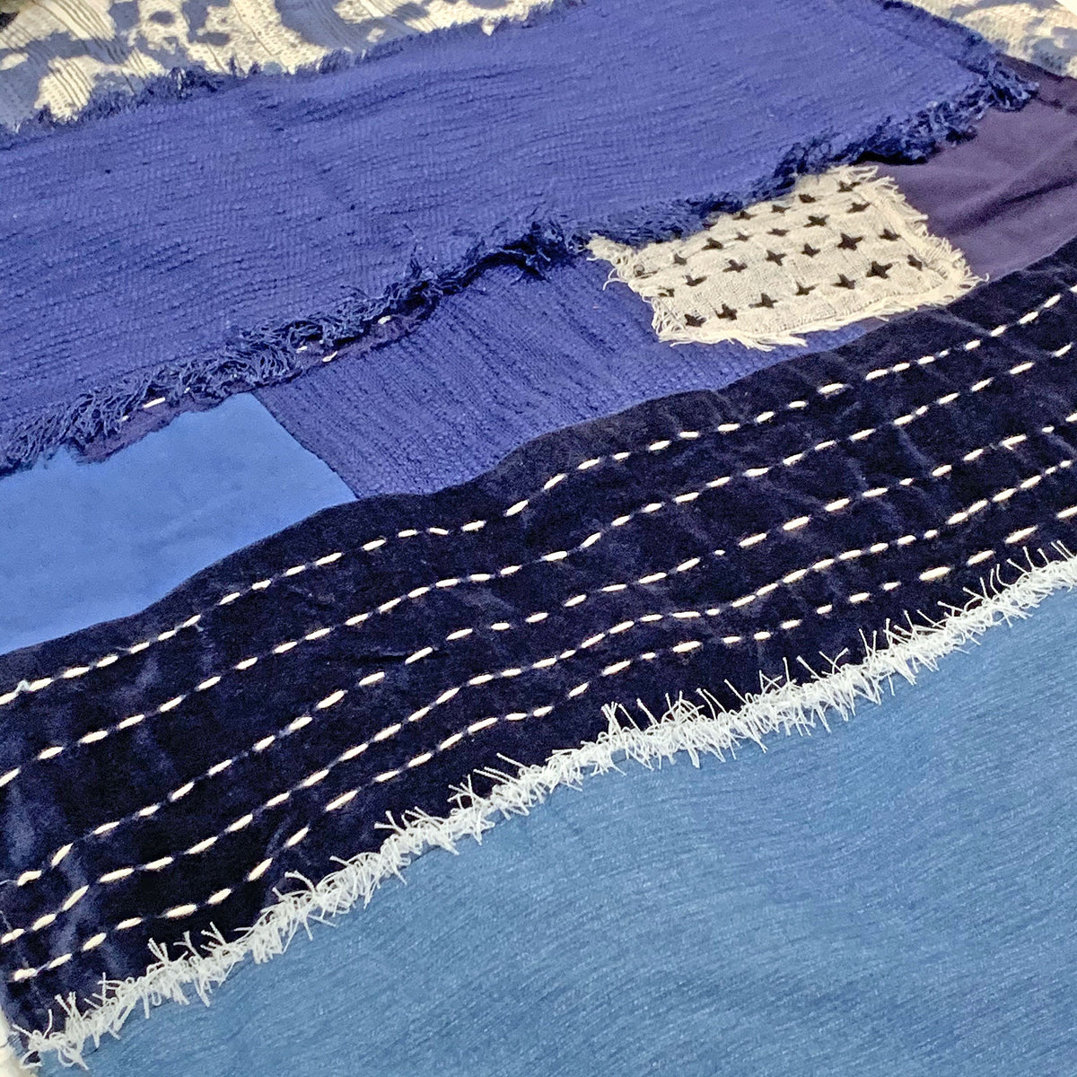 Detail of indigo dyed throw with white stitching across the indigo fabric