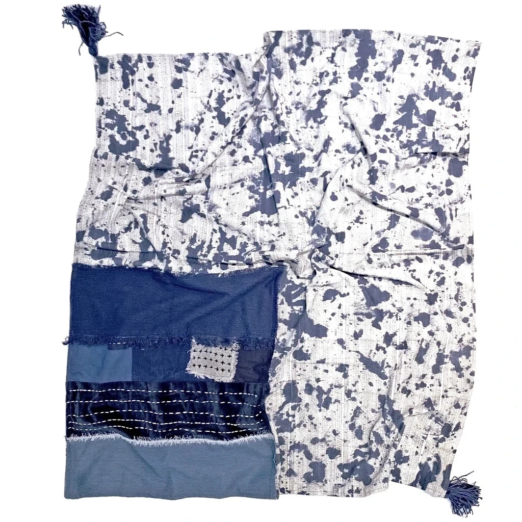 Reverse of indigo dyed throw. White with indigo splatters across the surface and blue tassels in the corners. 