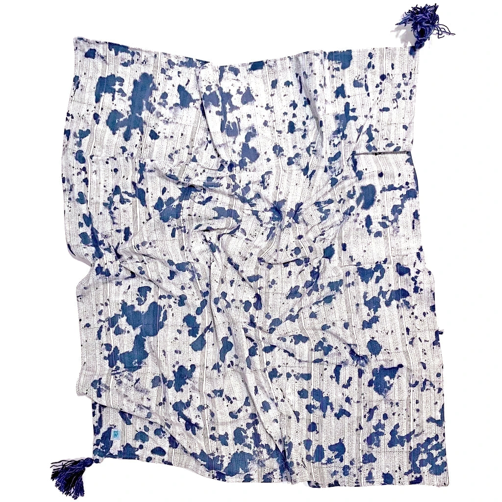 Reverse of indigo dyed throw. White with indigo splatters across the surface and blue tassels in the corners.